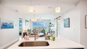 A modern kitchen with a large island, stainless steel sink, and overhead pendant lighting.