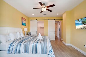 Ein Schlafzimmer mit Bett, Deckenventilator und einem Gemälde mit Strandmotiv.