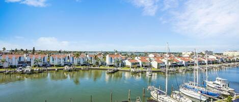 A marina with boats docked, a row of houses with red roofs, and a clear blue sky.