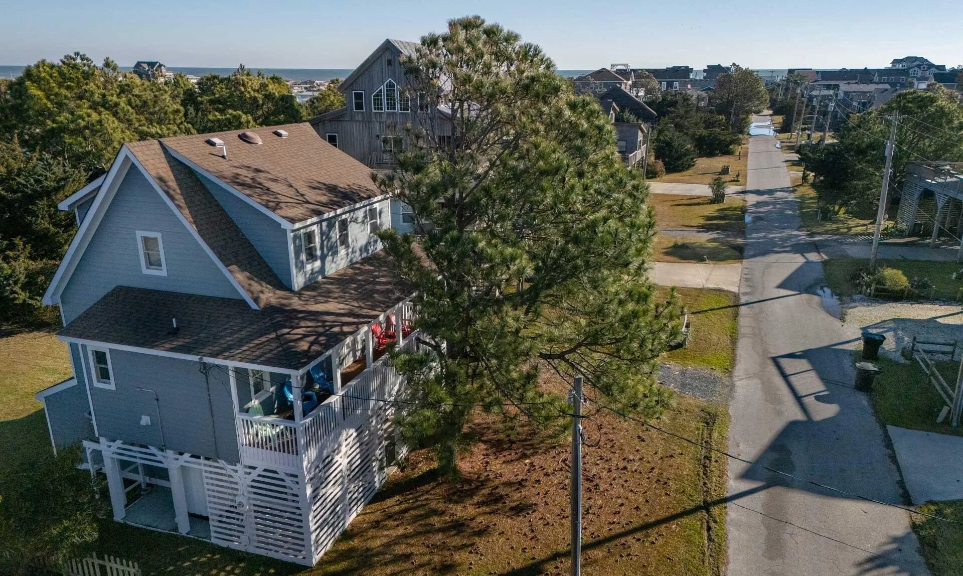 Une maison à deux étages avec un balcon, entourée d’arbres et offrant une vue dégagée sur l’océan.