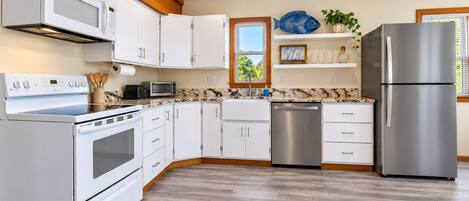 A modern kitchen with white cabinetry, stainless steel appliances, and a wooden floor.