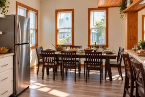 A kitchen with a stainless steel refrigerator, wooden dining table, and chairs. There are windows with blinds, and a plant is visible on the countertop. - Spacious, Dogs Welcome, 5-mins to Beach (Waves)