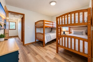 A room with bunk beds, a wooden desk, a potted plant, and a window.