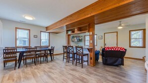 A spacious room with a wooden ceiling, a dining area with a table and chairs, a TV mounted on the wall, and a couch with a patterned throw.