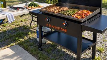 En portabel grill från BLACKSTONE med ett bord och tillhörande redskap, placerad på ett grusunderlag.