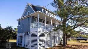 A two-story house with a balcony, surrounded by trees and a grassy yard.
