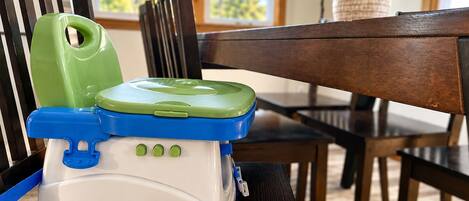 A portable child seat with a green and blue lid, placed on a wooden chair.