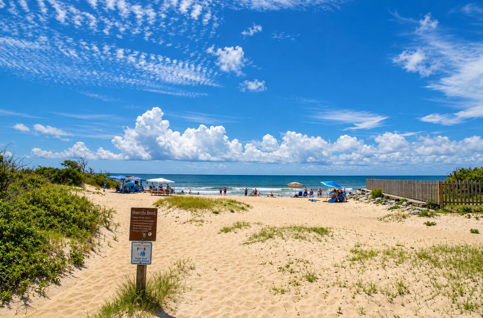 Ein Strand mit einem Schild, das eine 'Share the Beach'-Regelung anzeigt, einem Holzzaun und einem strahlend blauen Himmel.