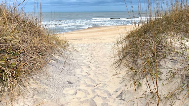 A sandy beach path leading to the ocean with overcast skies.