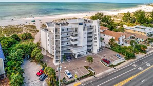 Ein mehrstöckiges Hotel mit Parkplatz in Strandnähe, mit Blick auf Meer und Sandstrand.
