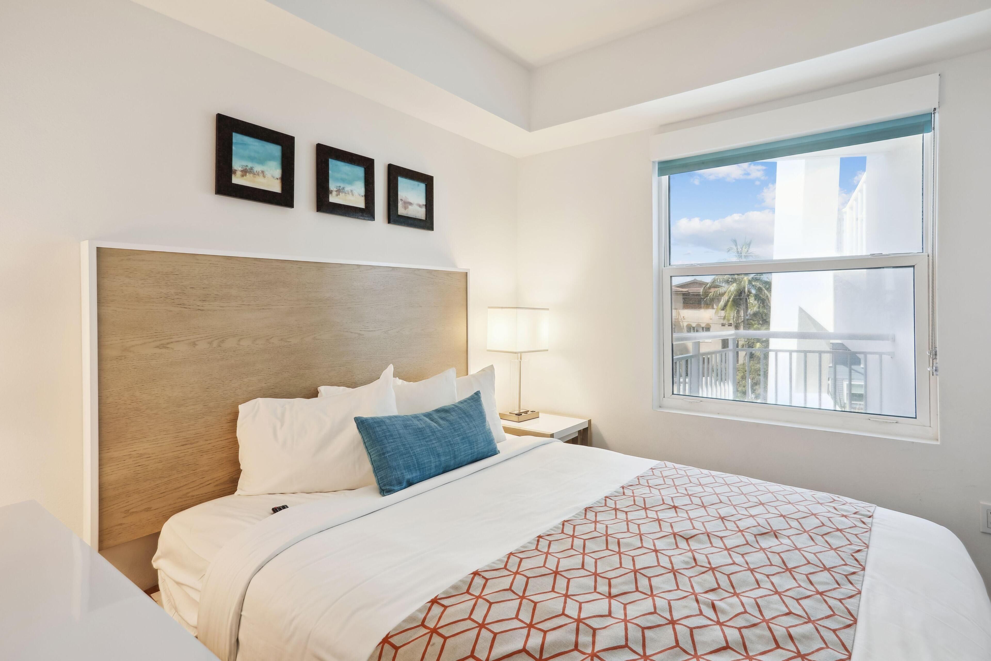 A hotel room with a large bed, a wooden headboard, a balcony with a railing, and three framed pictures on the wall.