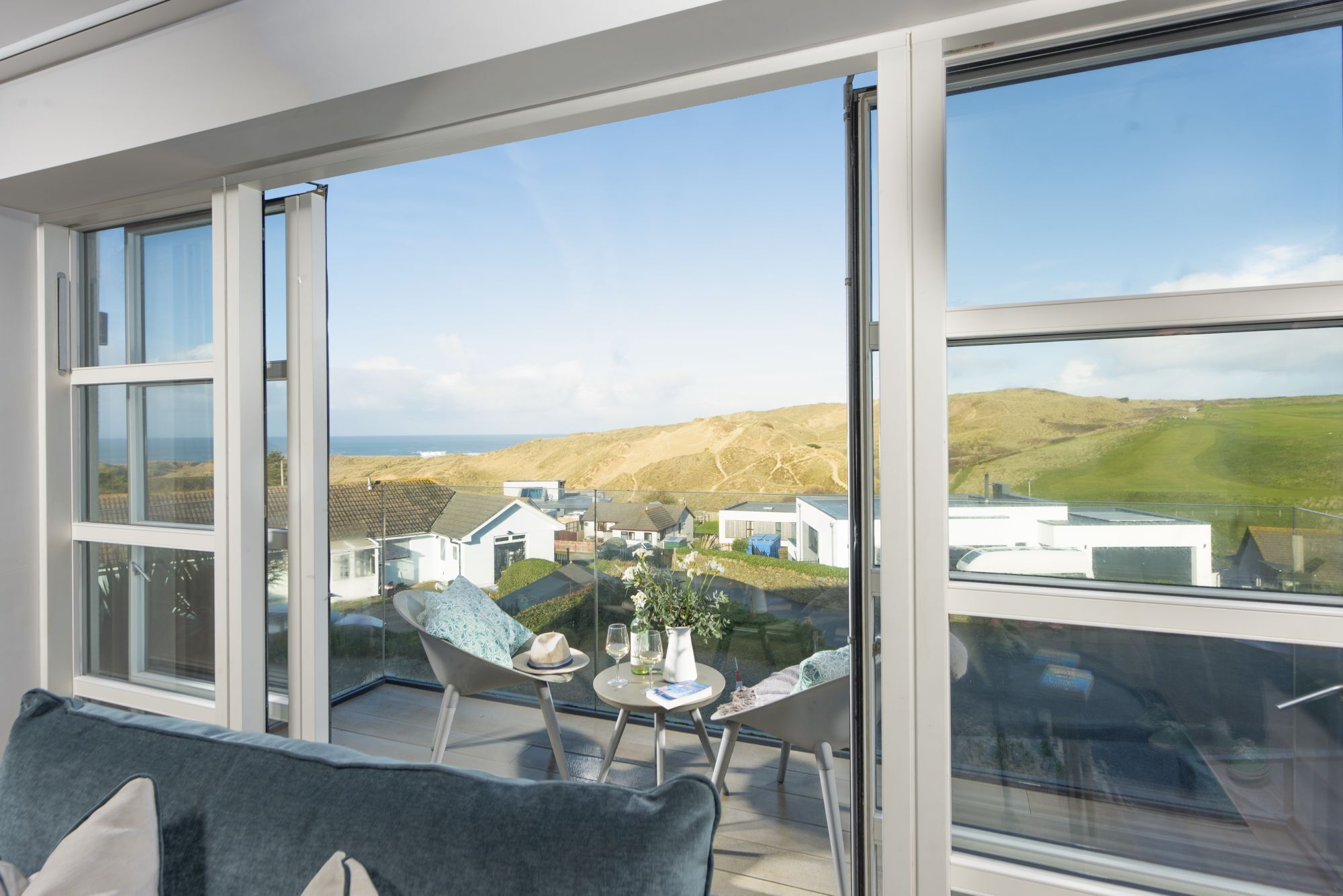 A modern room with large windows, a balcony, and a view of houses and hills.
