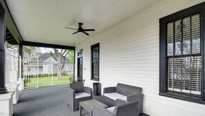 Eine überdachte Veranda mit Korbmöbeln, einem Deckenventilator und Blick auf ein Haus im Hintergrund.