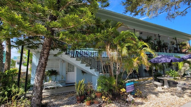 A two-story building with a staircase, outdoor seating area, and various plants. - Beach Quarters #2 (Gulfport)