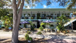 A beachfront hotel with a covered patio, outdoor seating, and a staircase leading to the upper level. - Beach Quarters #2 (Gulfport)