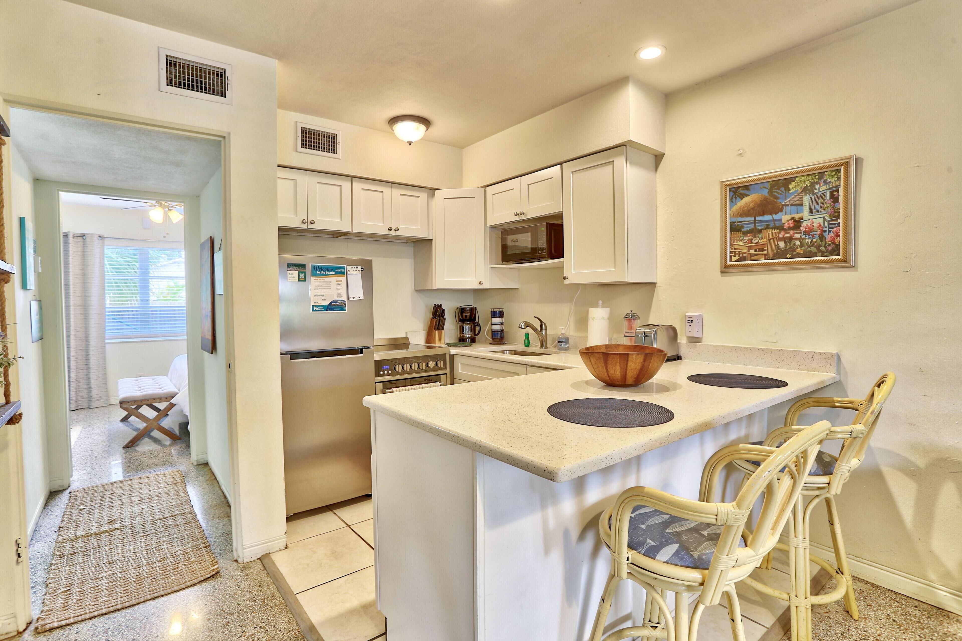 A kitchen with white cabinets, a microwave, a refrigerator, and a large island with bar stools.
