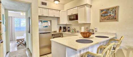 A kitchen with white cabinets, a microwave, a refrigerator, and a large island with bar stools.