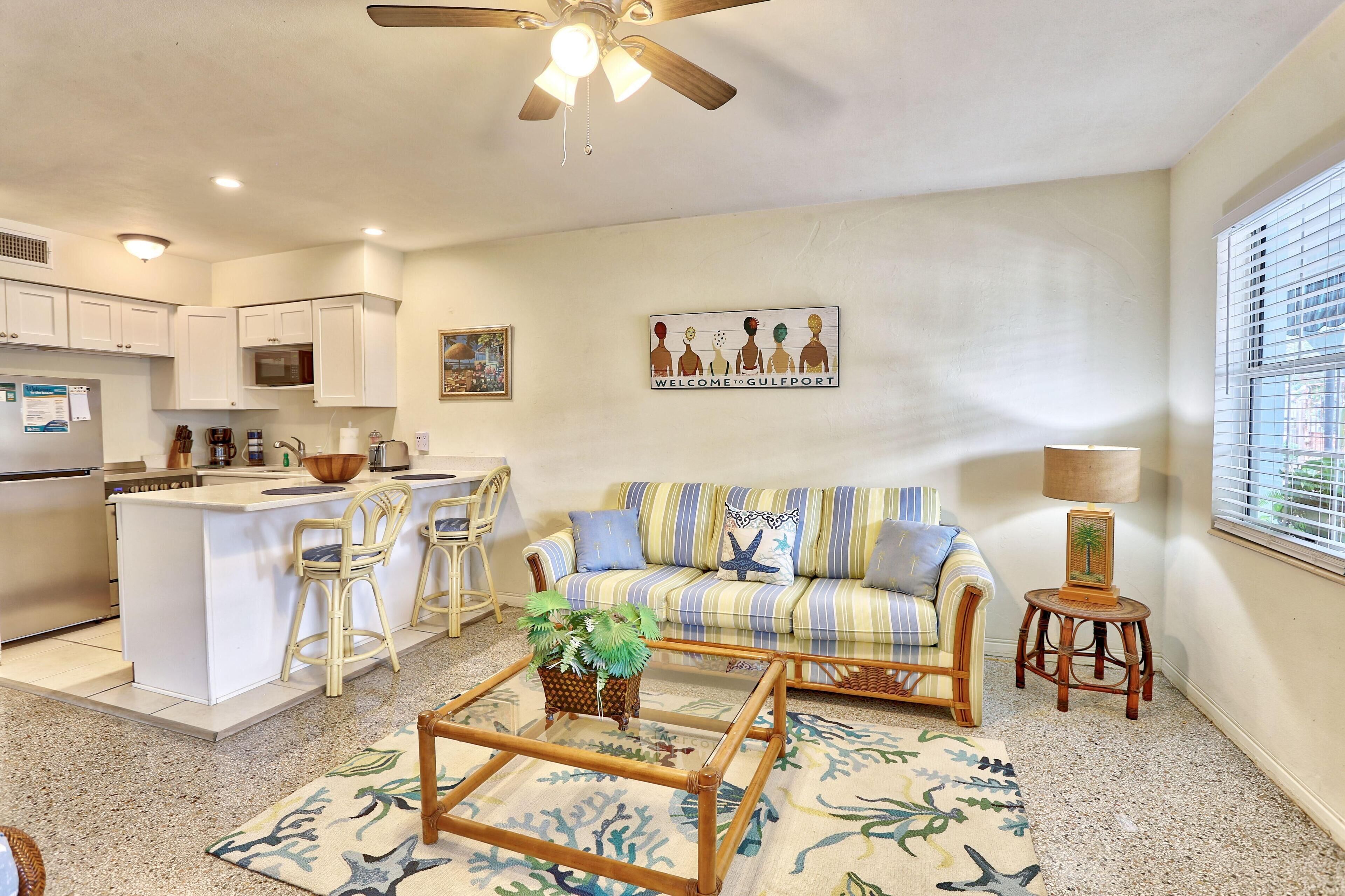 A modern kitchen with white cabinets, a central island with stools, a striped sofa, and a small side table with a lamp.