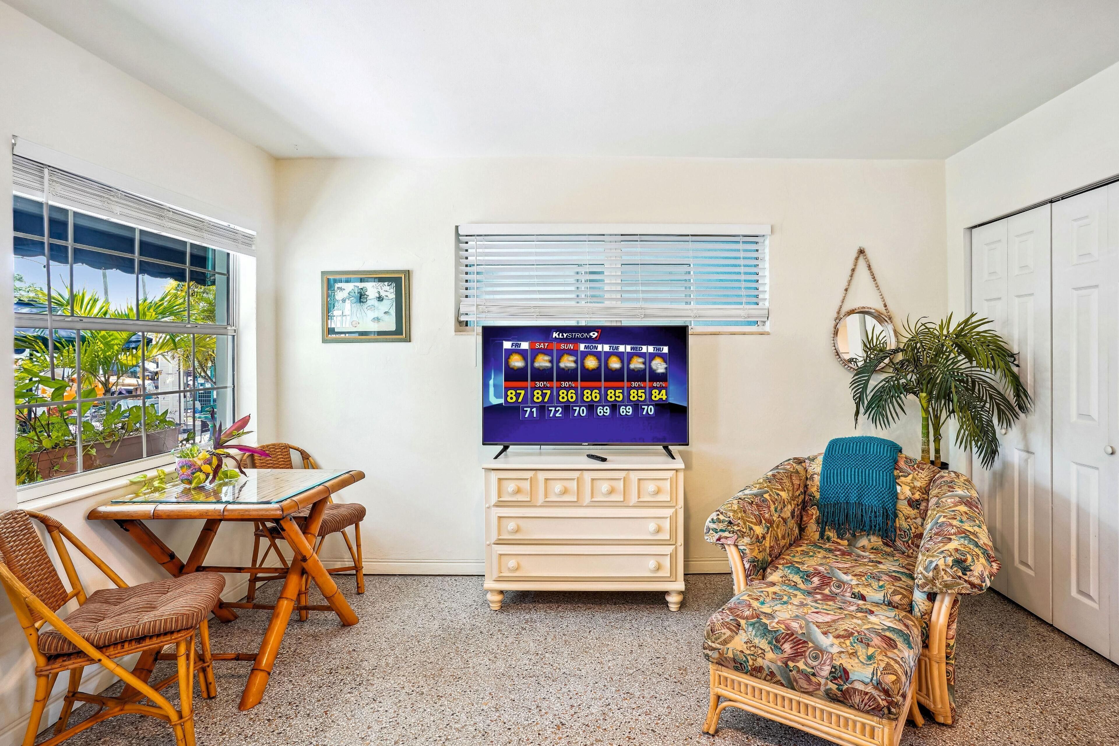 A room with a dining table, chairs, a TV, a sofa, and a potted plant.