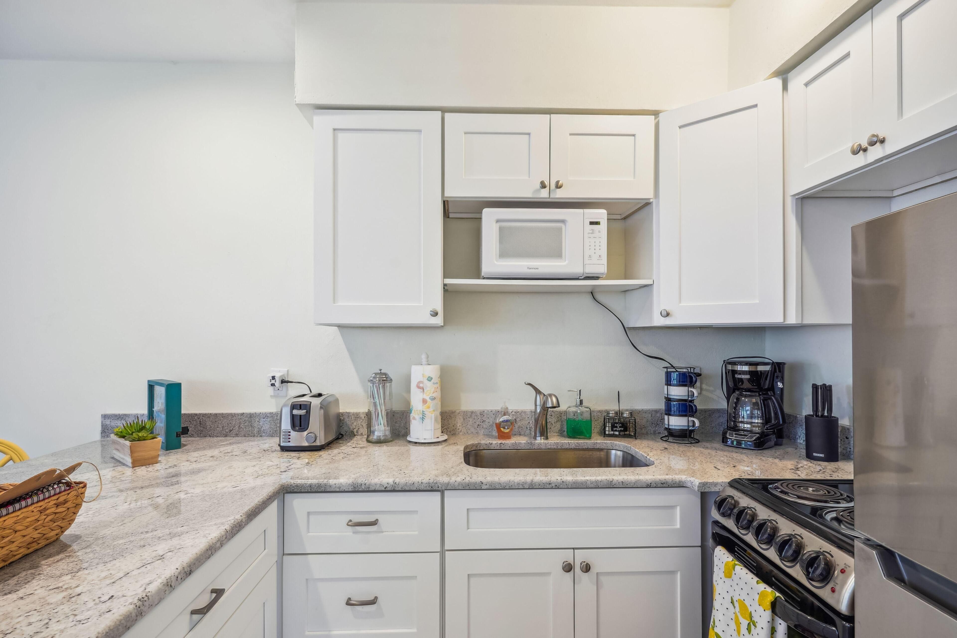 A modern kitchen with white cabinets, a microwave, a coffee maker, and a stove.