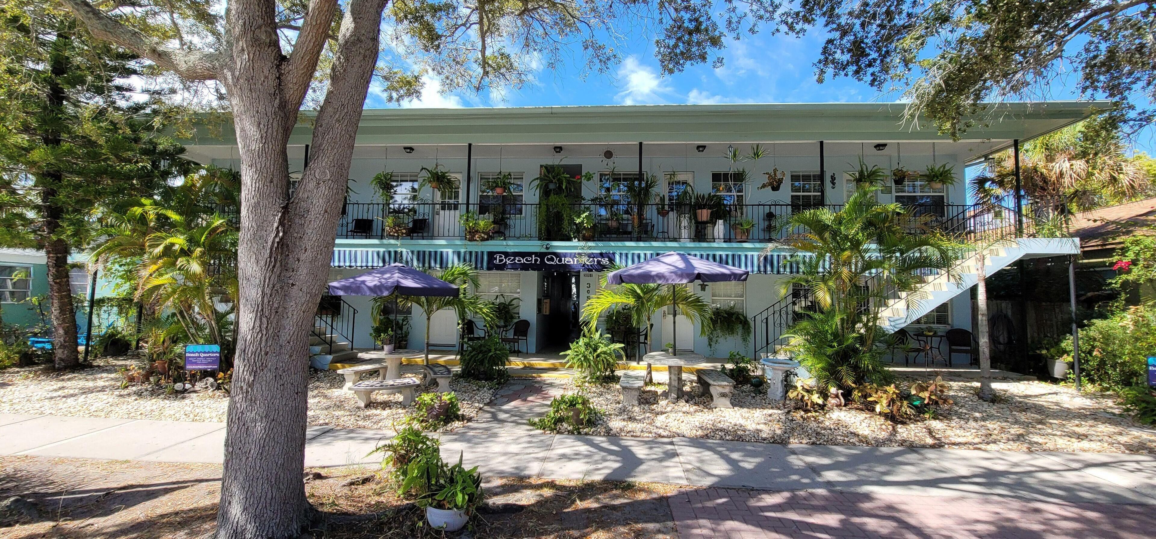 A beachfront hotel with a covered patio, outdoor seating, and a staircase leading to the upper level.