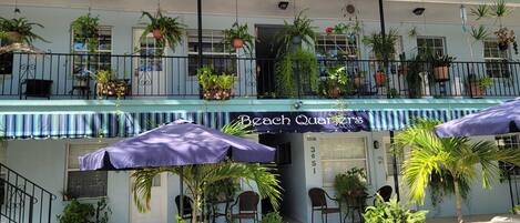 Um restaurante à beira-mar com área externa, plantas em vasos e uma placa com o texto 'Beach Quarters'.