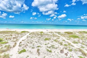 A beach with clear turquoise water, white sand, and sparse vegetation.