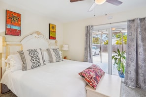 A bedroom with a large bed, decorative pillows, a ceiling fan, and a view of the outside.