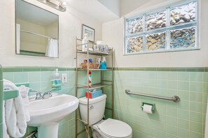 Casa de banho com lavatório, sanita e um prateleira com artigos de higiene pessoal.