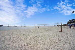 A sandy beach with a volleyball net, a small pavilion, and a clear sky.