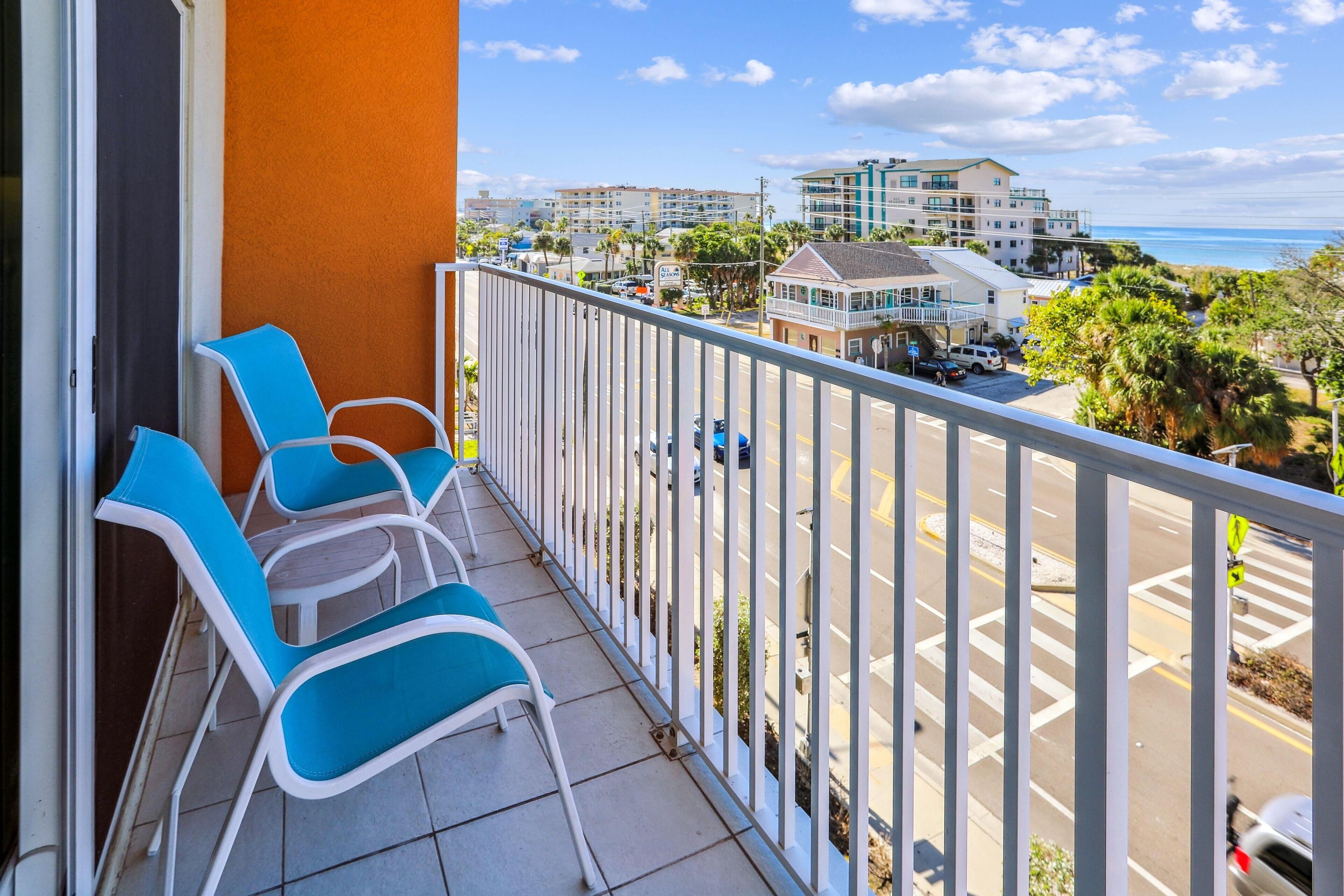 A balcony with blue chairs, a view of the street, and buildings in the background.