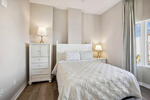 A bedroom with a bed, nightstands, a dresser, and a window with curtains. - Madeira Bay Resort I 1408 (Madeira Beach)