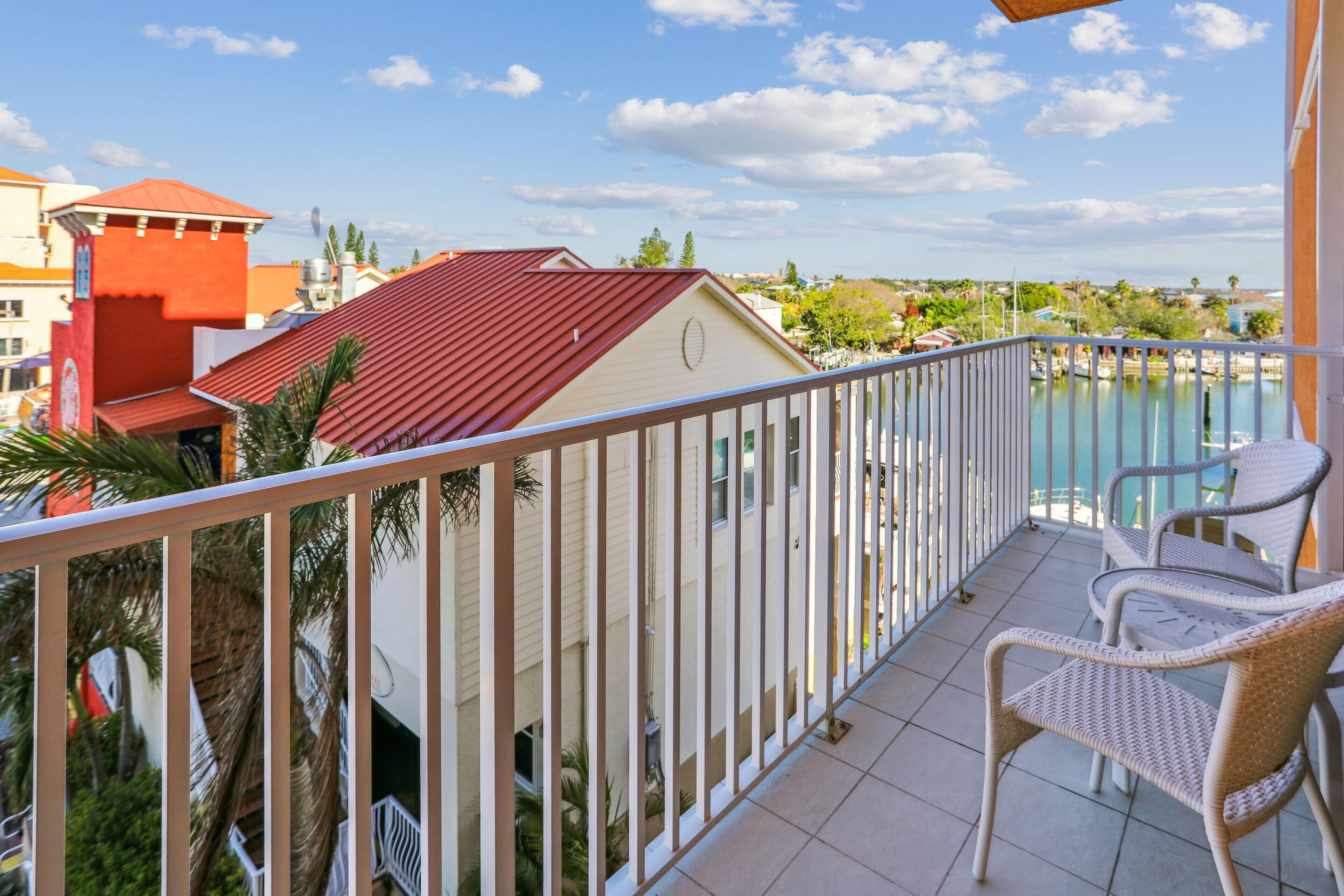 A balcony with white wicker chairs, a view of a marina, and buildings with red roofs.