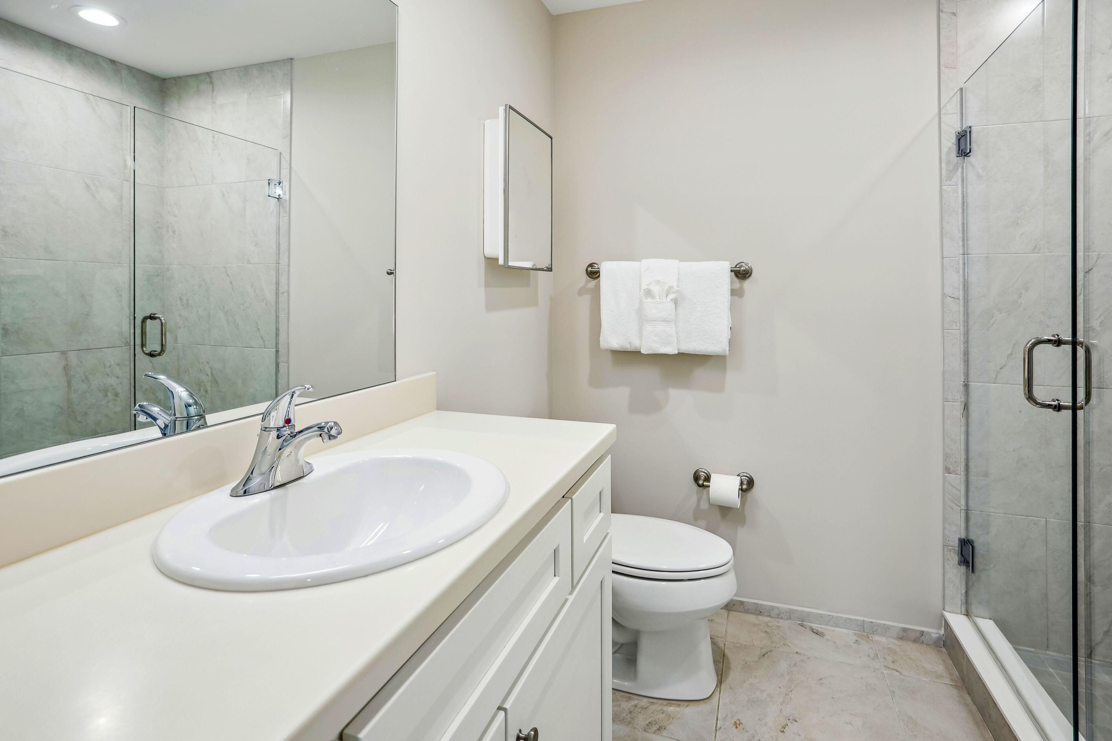 Ein modernes Badezimmer mit Waschbecken, Spiegel, Toilette und Duschkabine aus Glas.