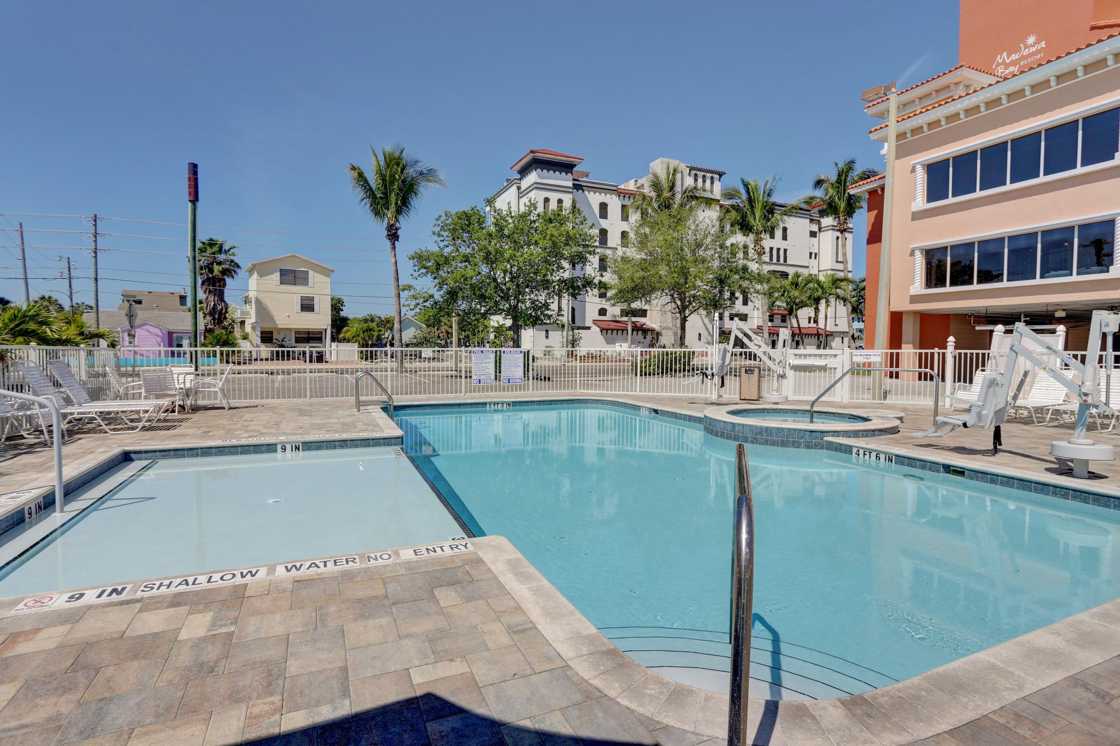 Una piscina con un cartel de agua poco profunda, rodeada de sillas de descanso y un edificio con un letrero que dice "Marriott".