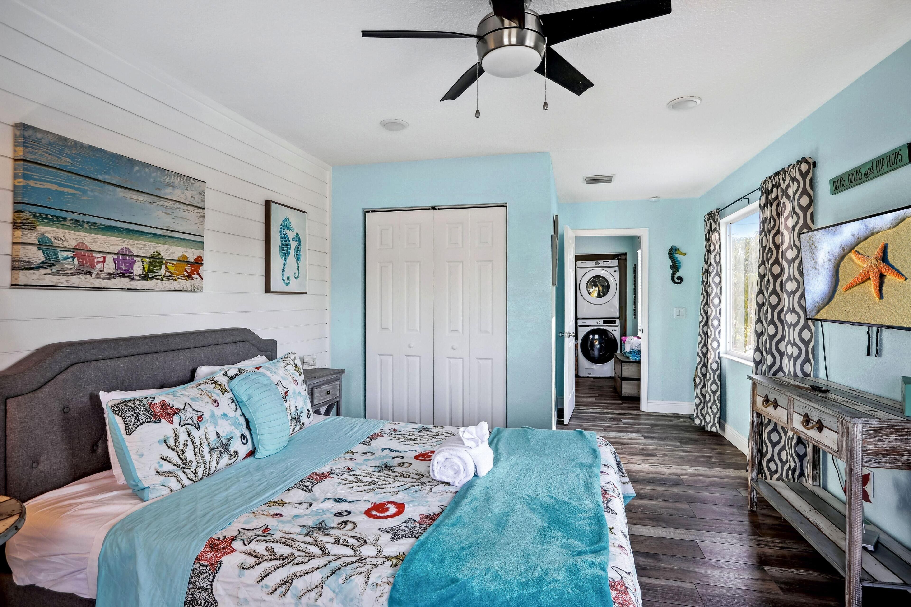 Un dormitorio con cama, ventilador de techo, una puerta, zona de lavandería y un muro decorado con una decoración de caballito de mar.