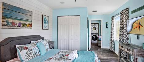 Un dormitorio con cama, ventilador de techo, una puerta, zona de lavandería y un muro decorado con una decoración de caballito de mar.