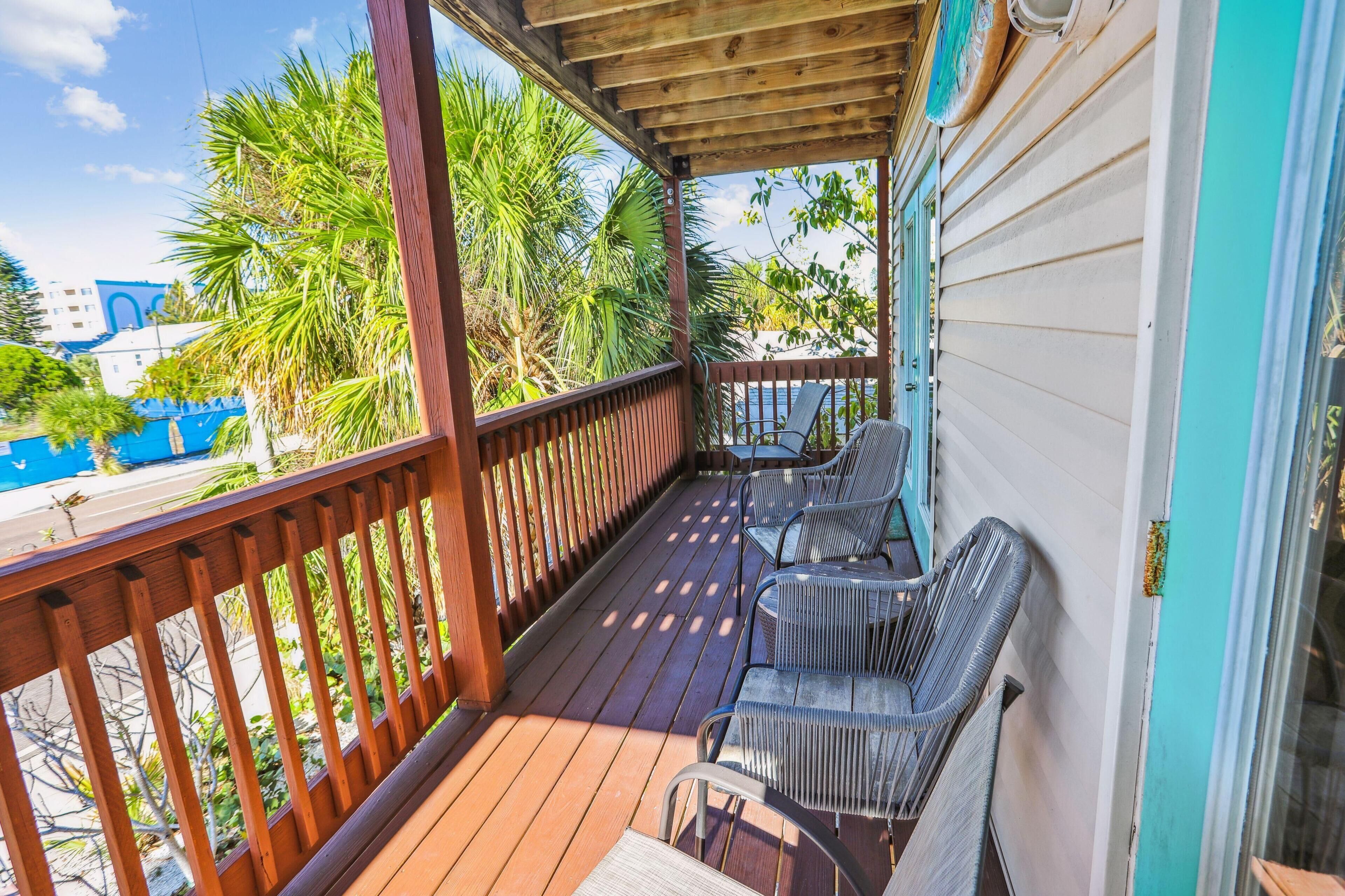 A wooden deck with outdoor furniture, a view of palm trees, and a building in the background.