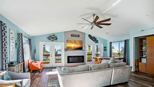 A living room with a fireplace, a ceiling fan, and a large TV. - Beach Life 5 (Treasure Island)