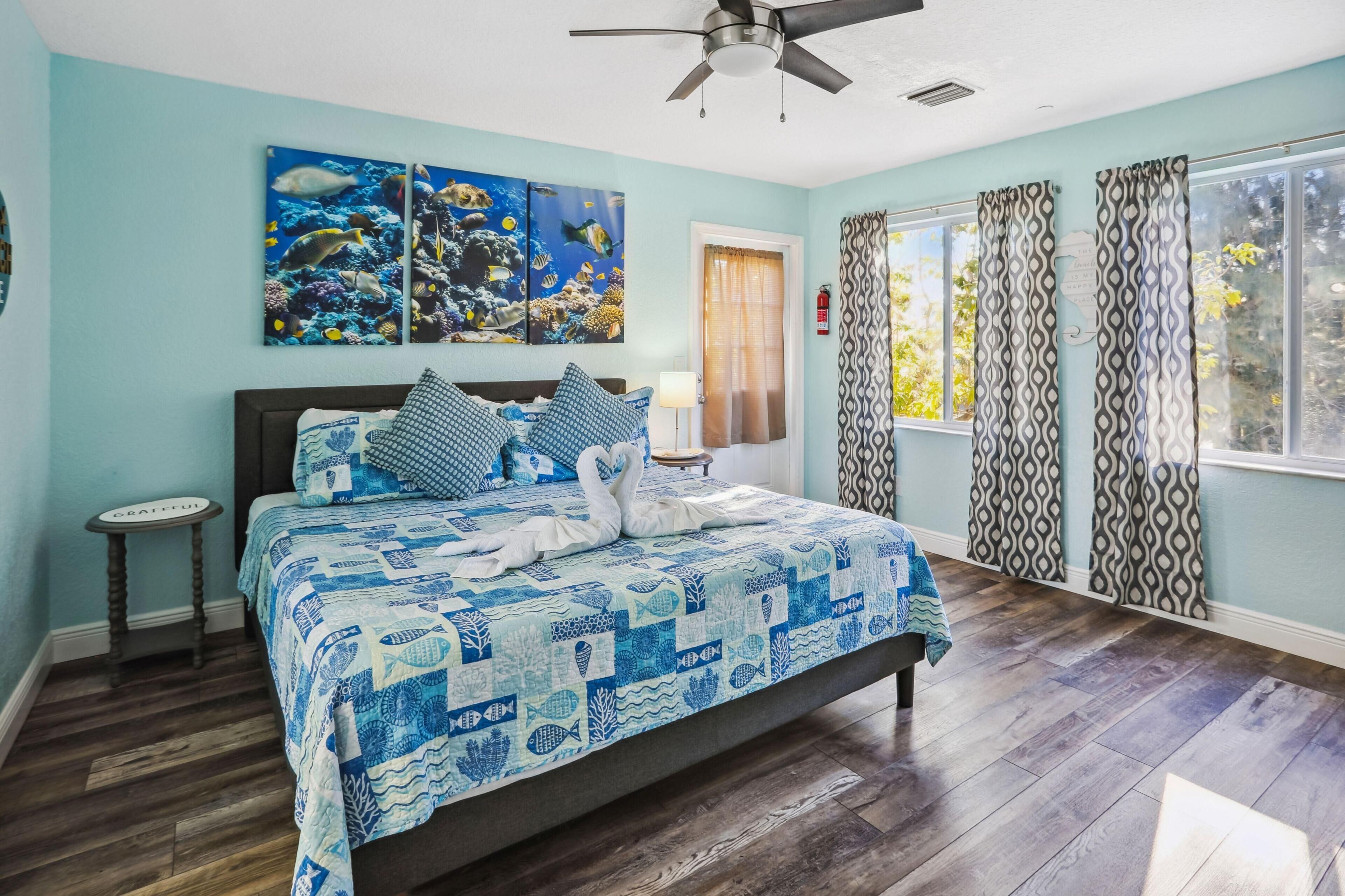 A bedroom with a bed, a ceiling fan, a window with curtains, and artwork on the wall.