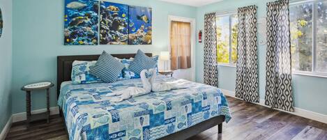 A bedroom with a bed, a ceiling fan, a window with curtains, and artwork on the wall.