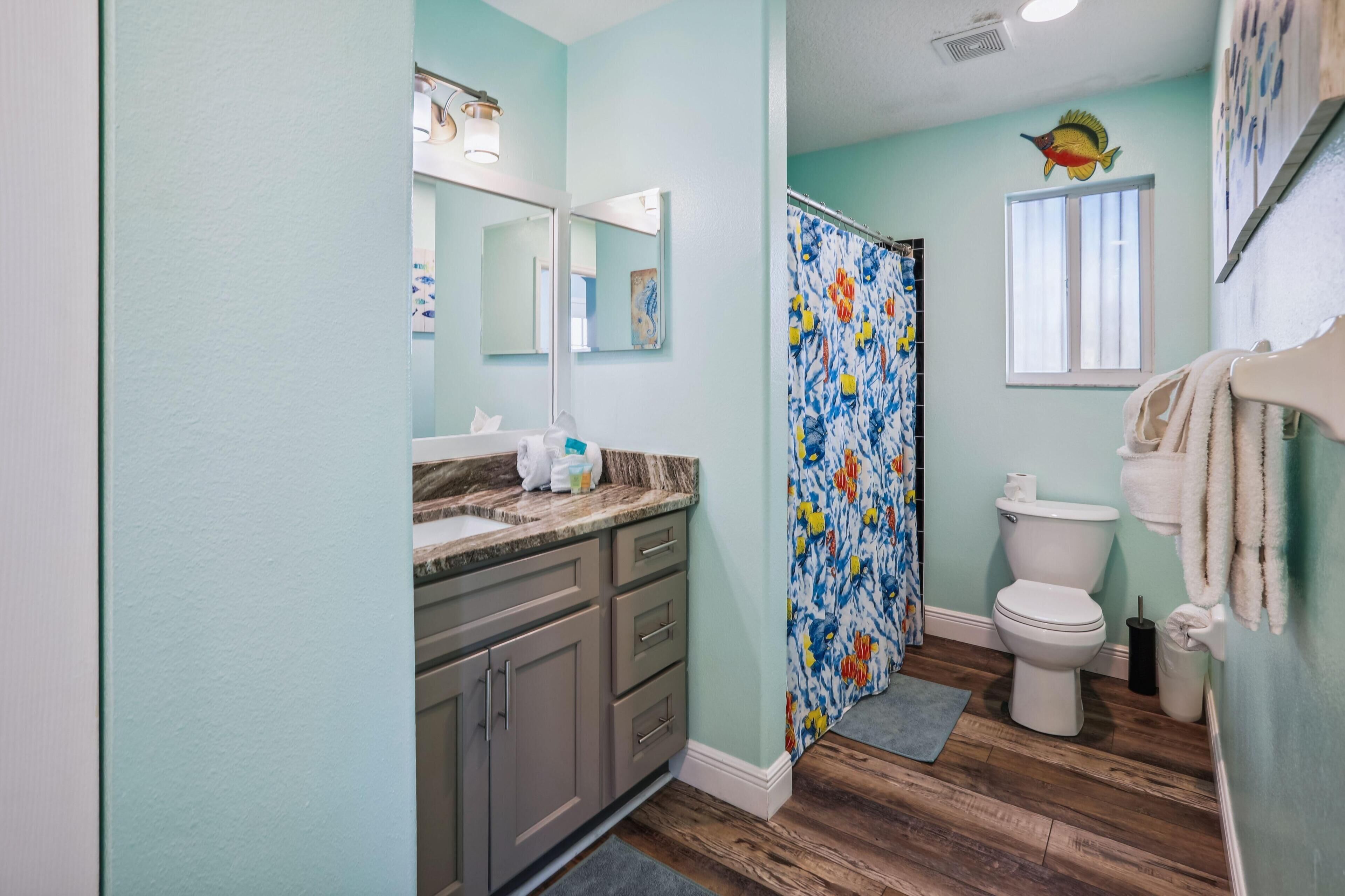 A bathroom with a shower curtain, toilet, and a sink with a mirror.