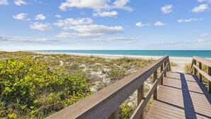 A wooden boardwalk leading to a beach with clear skies and sparse vegetation. - Beach Life 5 (Treasure Island)