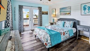 A bedroom with a bed, a desk, a ceiling fan, and a view through a door. - Beach Life 5 (Treasure Island)