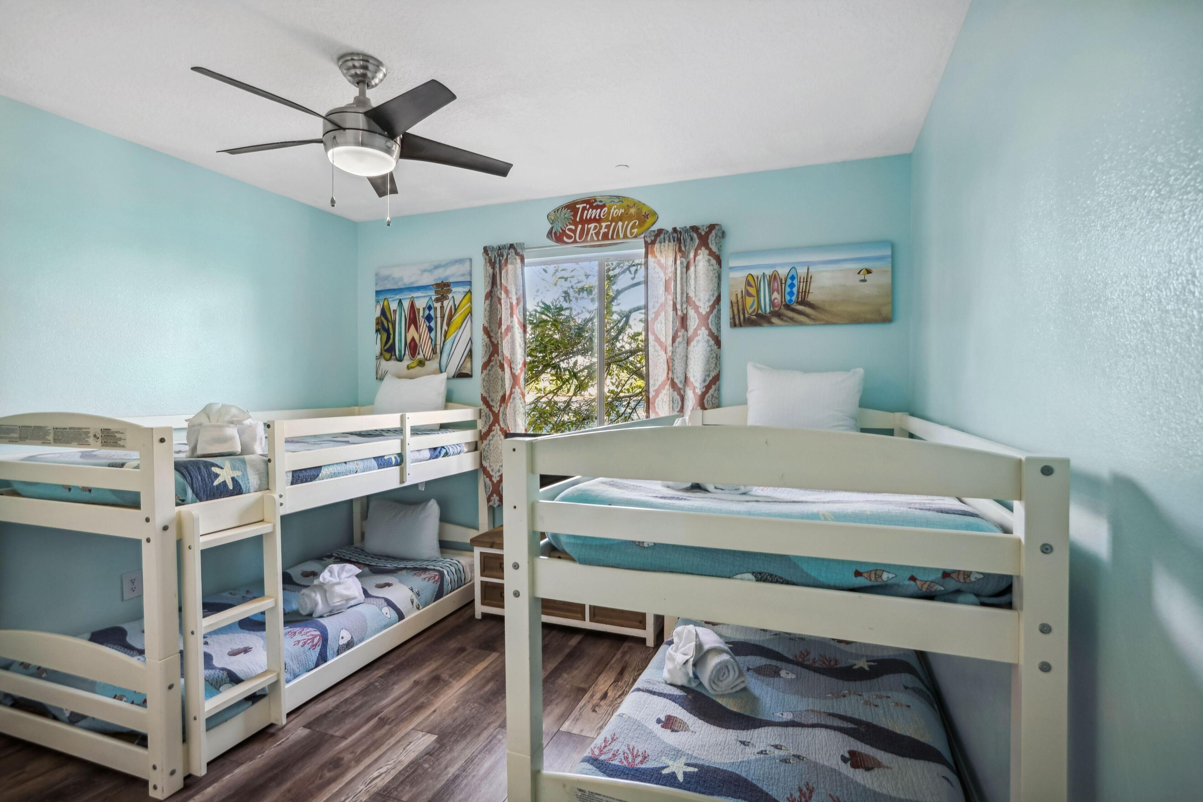 A room with bunk beds, a ceiling fan, a window with curtains, and a painting on the wall.
