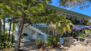 A two-story building with a staircase, outdoor seating area, and various plants. - Beach Quarters 2BR #5 and #6 (Gulfport)