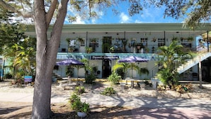 A beachfront hotel with a covered patio, outdoor seating, and a staircase leading to the upper level. - Beach Quarters 2BR #5 and #6 (Gulfport)
