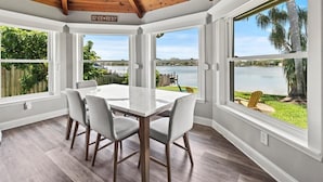 A dining area with a table and chairs, large windows with a view of a lake, and a wooden ceiling.