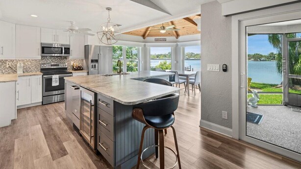 A modern kitchen with a large island, stainless steel appliances, and a view of a lake through large sliding glass doors.