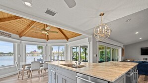 A spacious kitchen with a large island, wooden ceiling, and a view of a body of water.